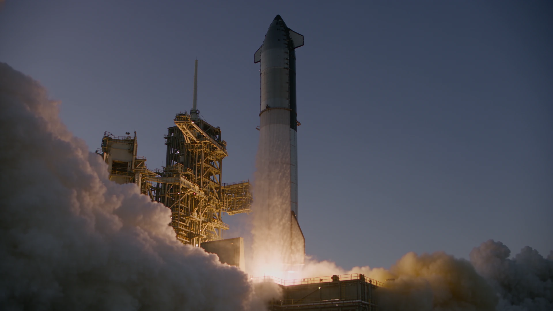 An orbital launch vehicle rising above the pad in a plume of fire and vapor; illustrative mission film